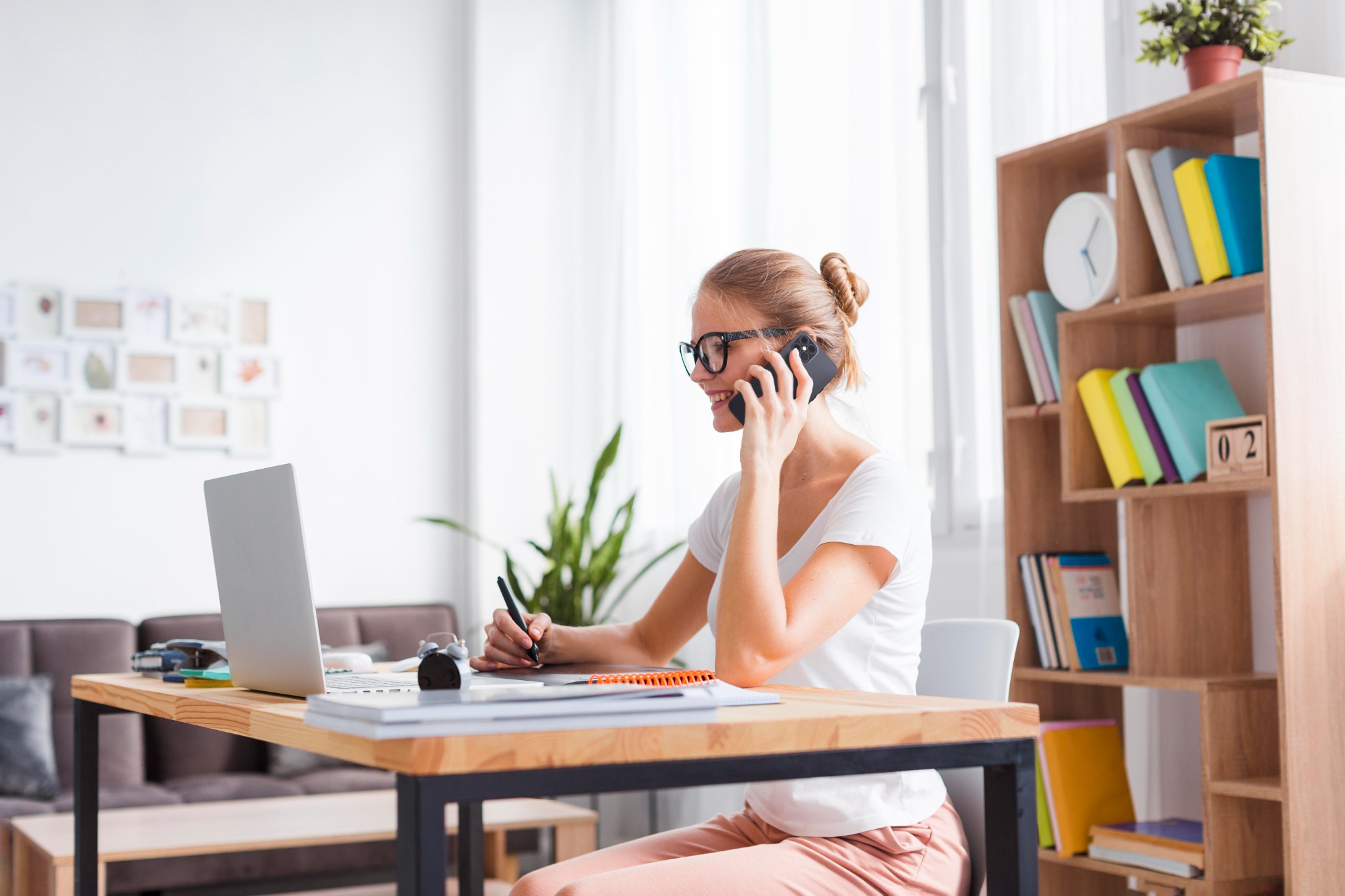 Thuiswerkende vrouw belt met haar telefoon aan een bureau met laptop